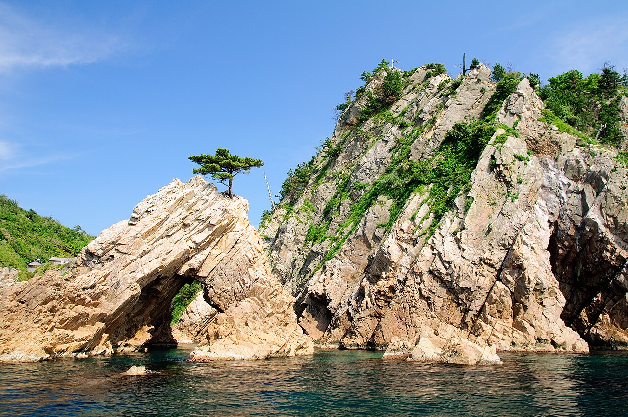 A rock islet topped by a single bent pine off the Uradome coast of Tottori, rising from clear green water.