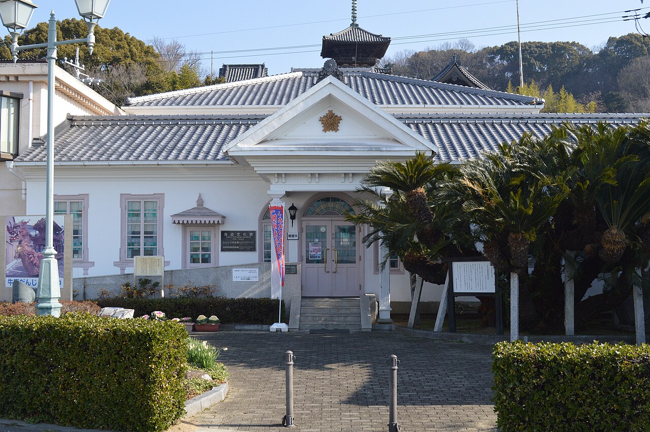 The white Western-style front of the Kaiyu Cultural Museum in Ushimado, a former police station with a gabled porch, pale tiled roof and cycad palms beside the path