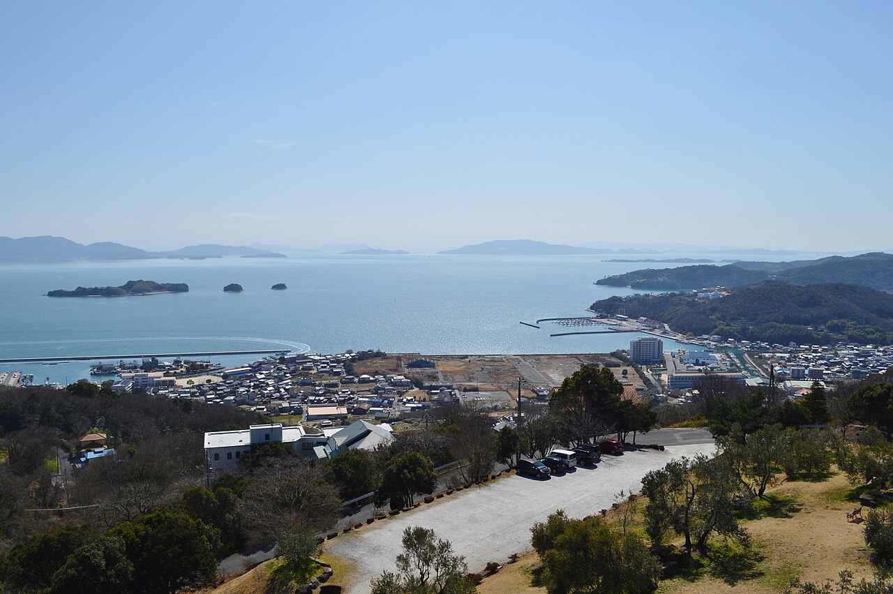 A view over Ushimado Bay from the hillside Olive Garden: small islands on a calm blue sea, the harbour breakwater, and the town's tiled rooftops below