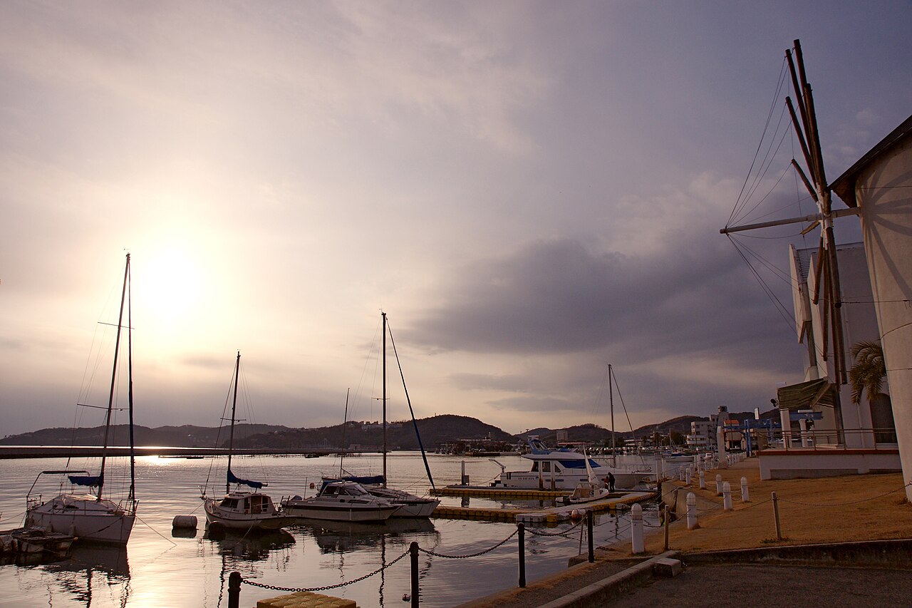 Yachts moored at Ushimado Port at dusk, with the sun low over the water and a white windmill-shaped building on the right