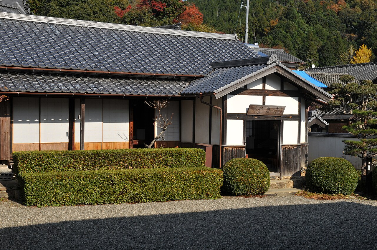 The single-storey, white-walled Shingido private school building with a tiled roof and clipped hedges beside a gravel courtyard in Seiyo.