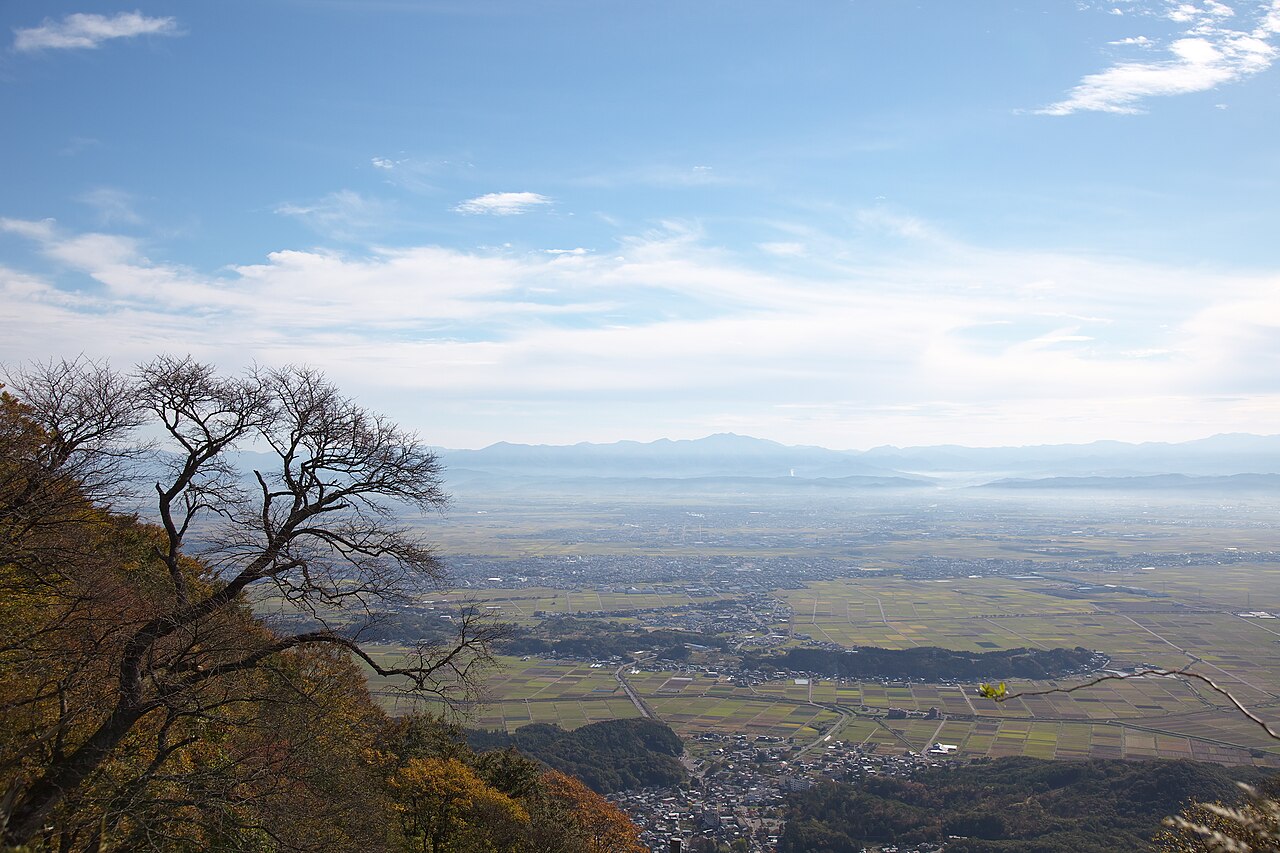 A view from Mount Yahiko over the Echigo plain, with fields, town buildings and distant mountain ranges
