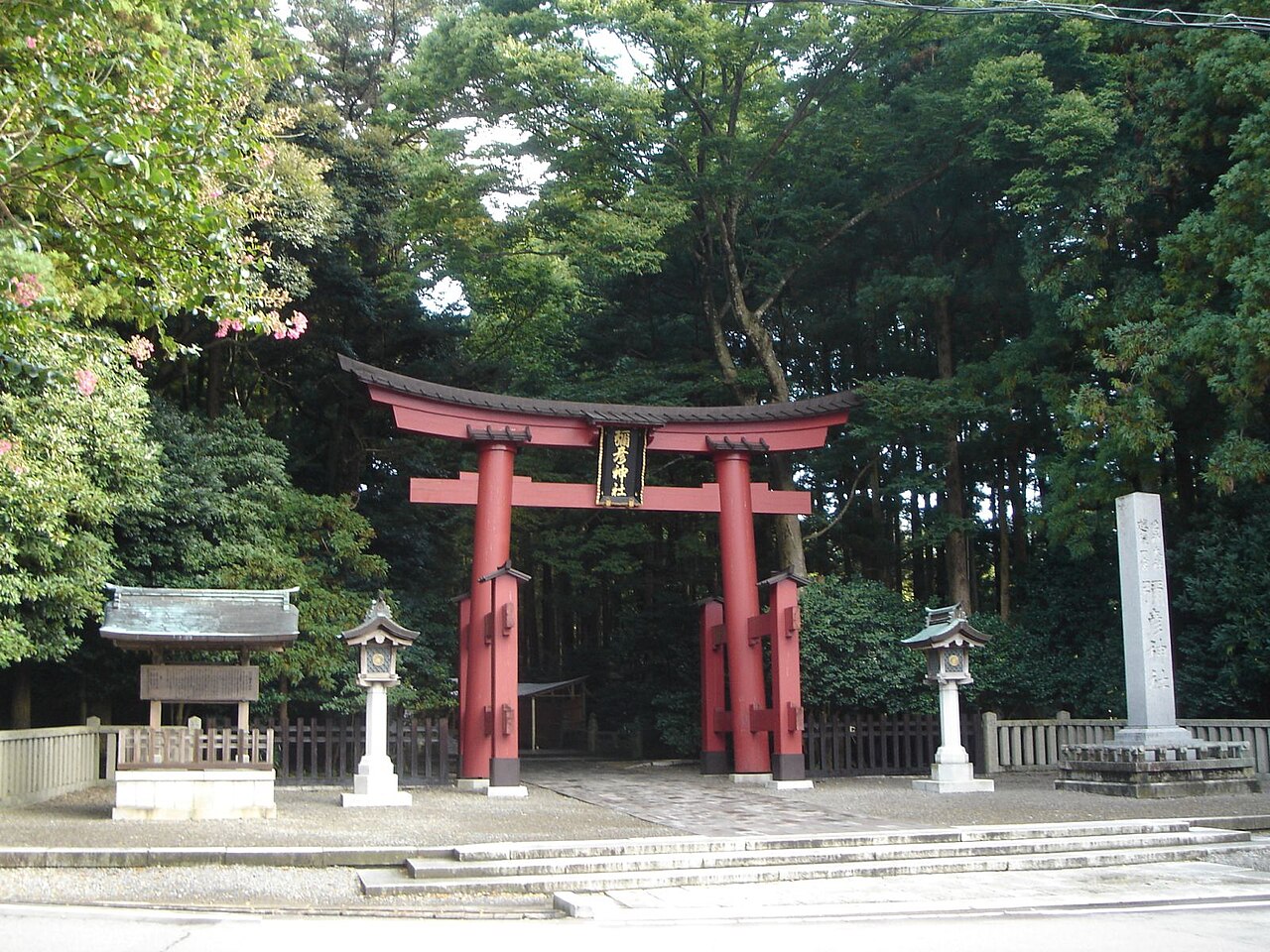 A vermilion torii gate among trees, with stone lanterns on both sides