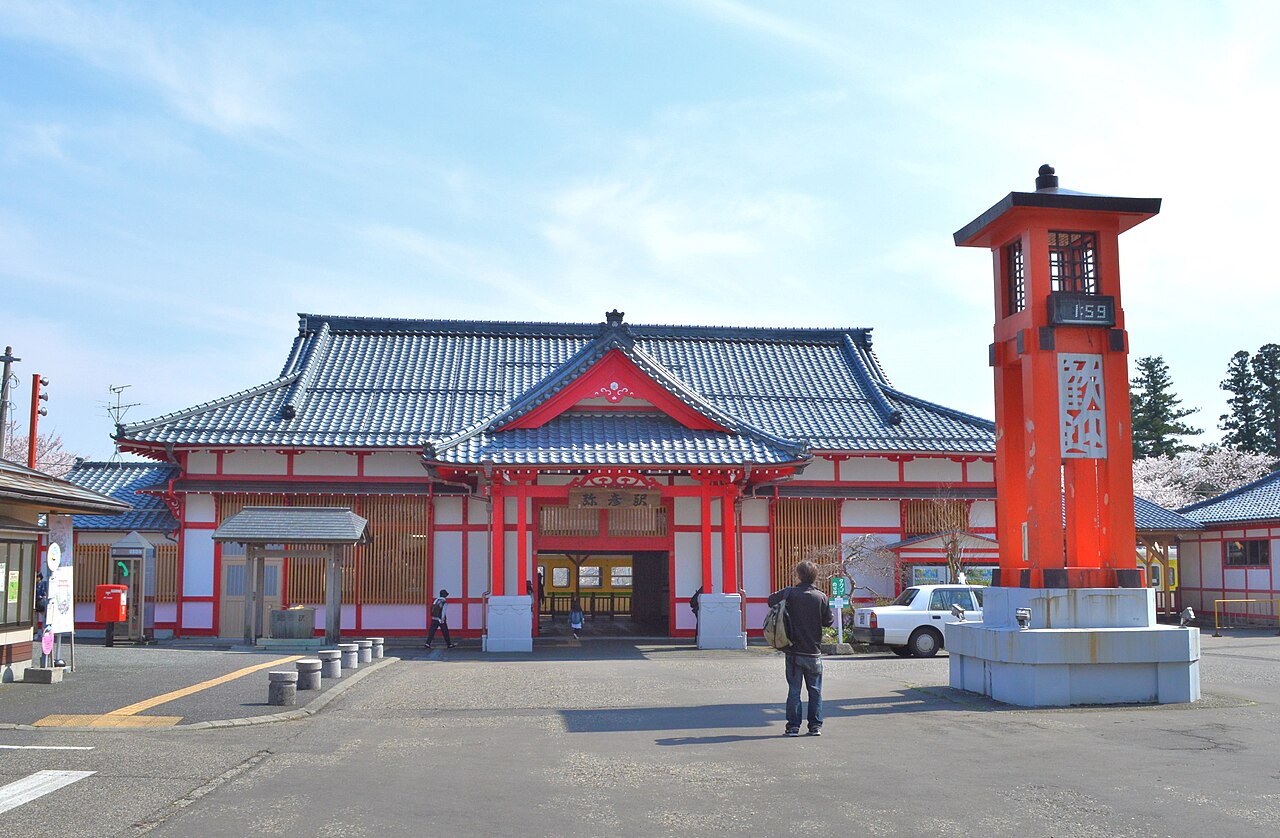 Yahiko Station building with red trim and a tiled roof, beside a red lantern-shaped tower