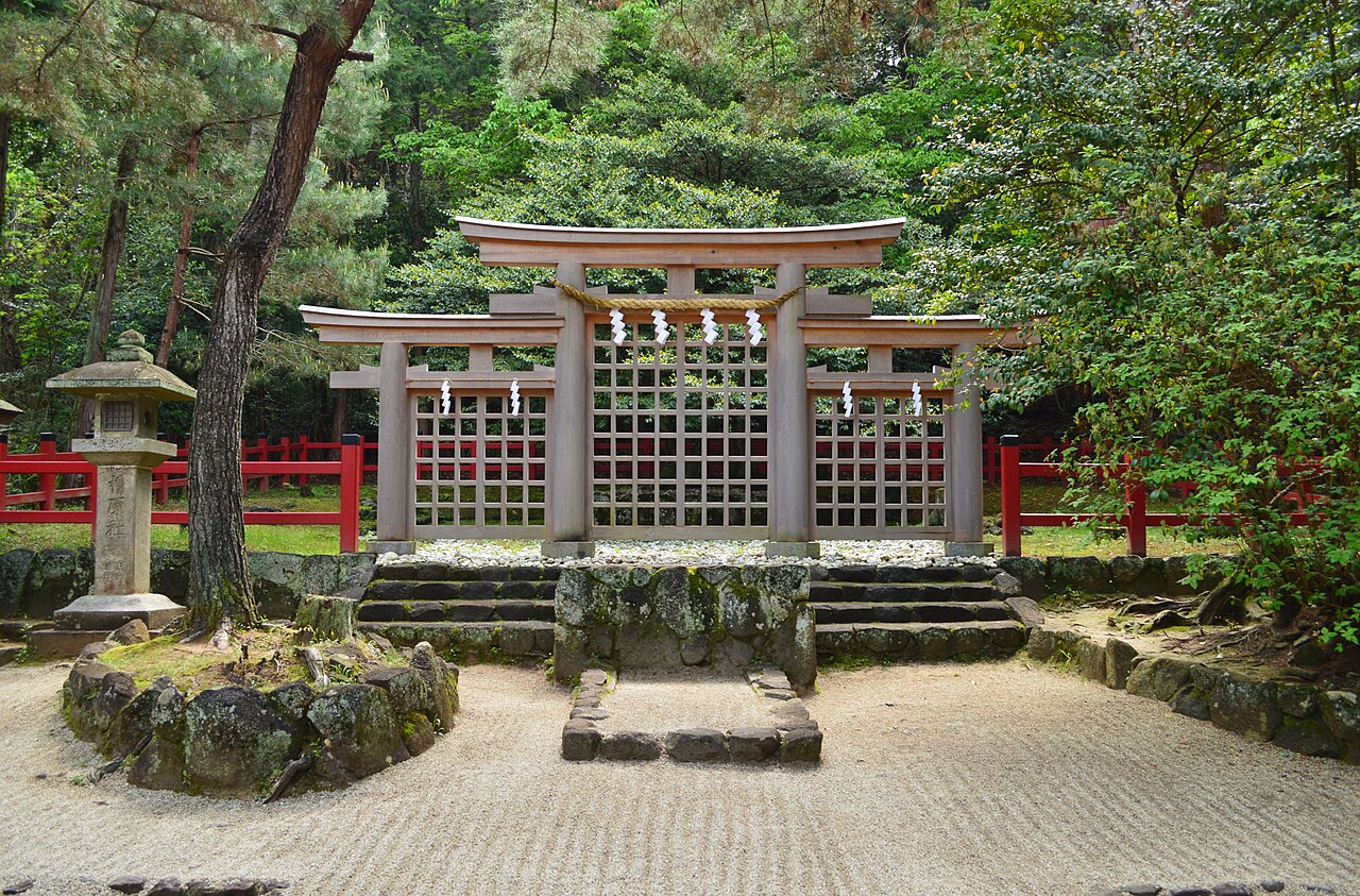 Triple torii framing a lattice fence and a small gravel shrine area among pine trees at Hibara Shrine, with a stone lantern at left