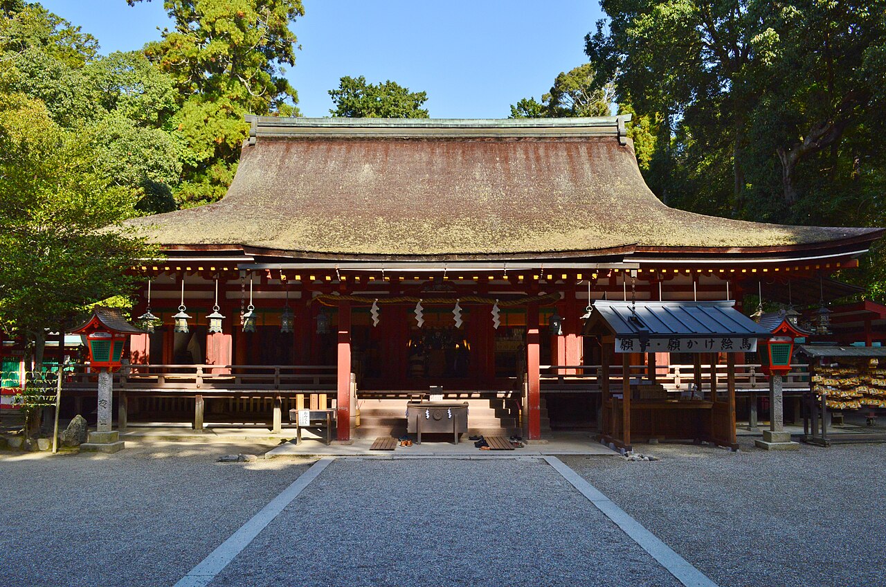 Wide cypress-bark-roofed worship hall of Isonokami Shrine with red pillars and hanging lanterns, seen across a gravel forecourt