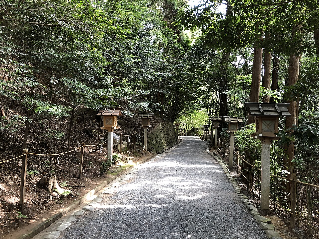 Wide gravel path running between wooded banks with stone markers on both sides, part of the Yamanobe no Michi between Sai Shrine and Omiwa Shrine