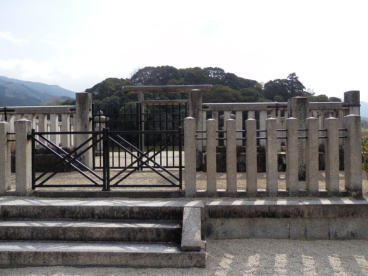 Stone-fenced worship gate in front of the wooded mound traditionally identified as the tomb of Emperor Sujin, with the Yamato hills behind