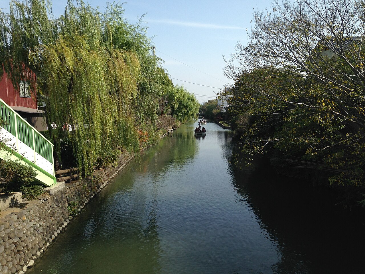 A narrow canal lined with willow trees in Yanagawa, with a boat in the distance