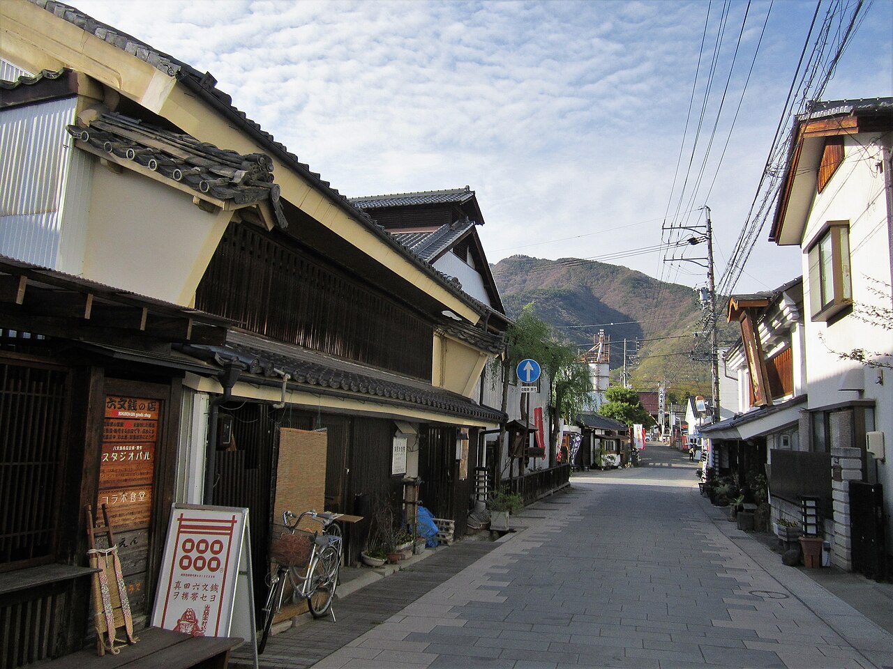 The paved lane of Yanagimachi with old wooden shopfronts on both sides and a hill at the far end
