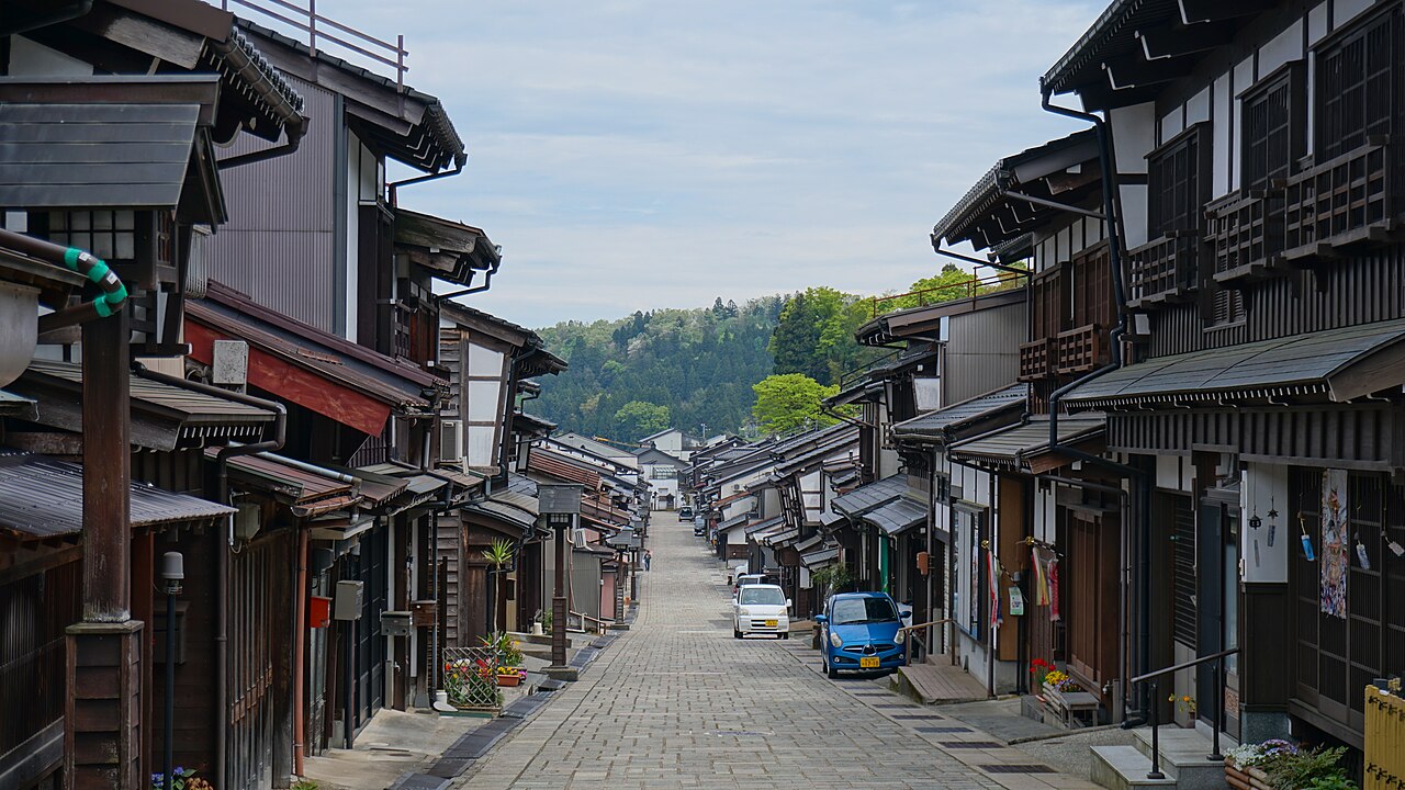 Stone-paved Suwamachi Hondori street in Yatsuo, lined with old wooden machiya townhouses and leading toward forested hills.