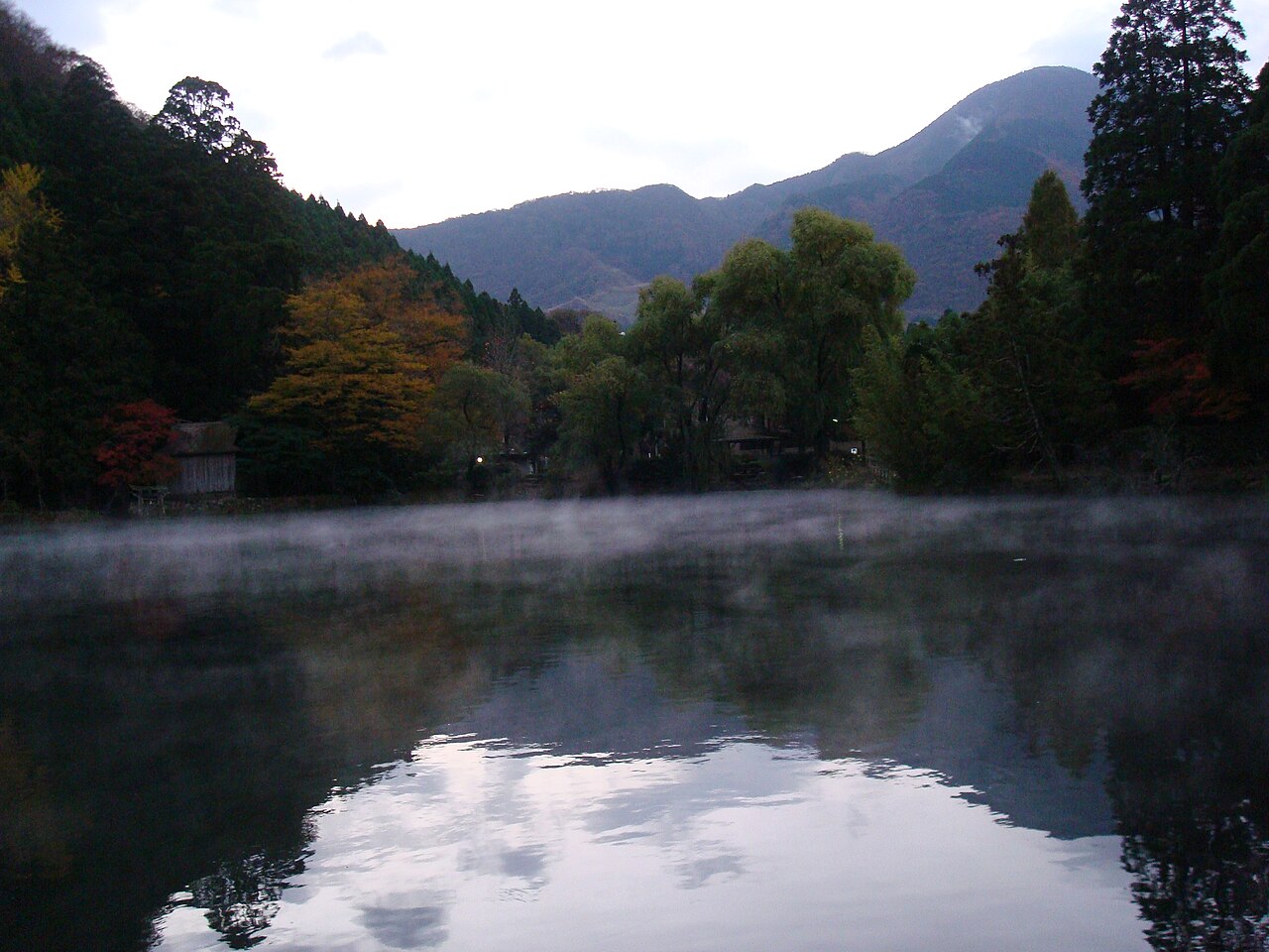Low mist drifting across the dark surface of Lake Kinrin at dawn, with autumn trees and mountains behind