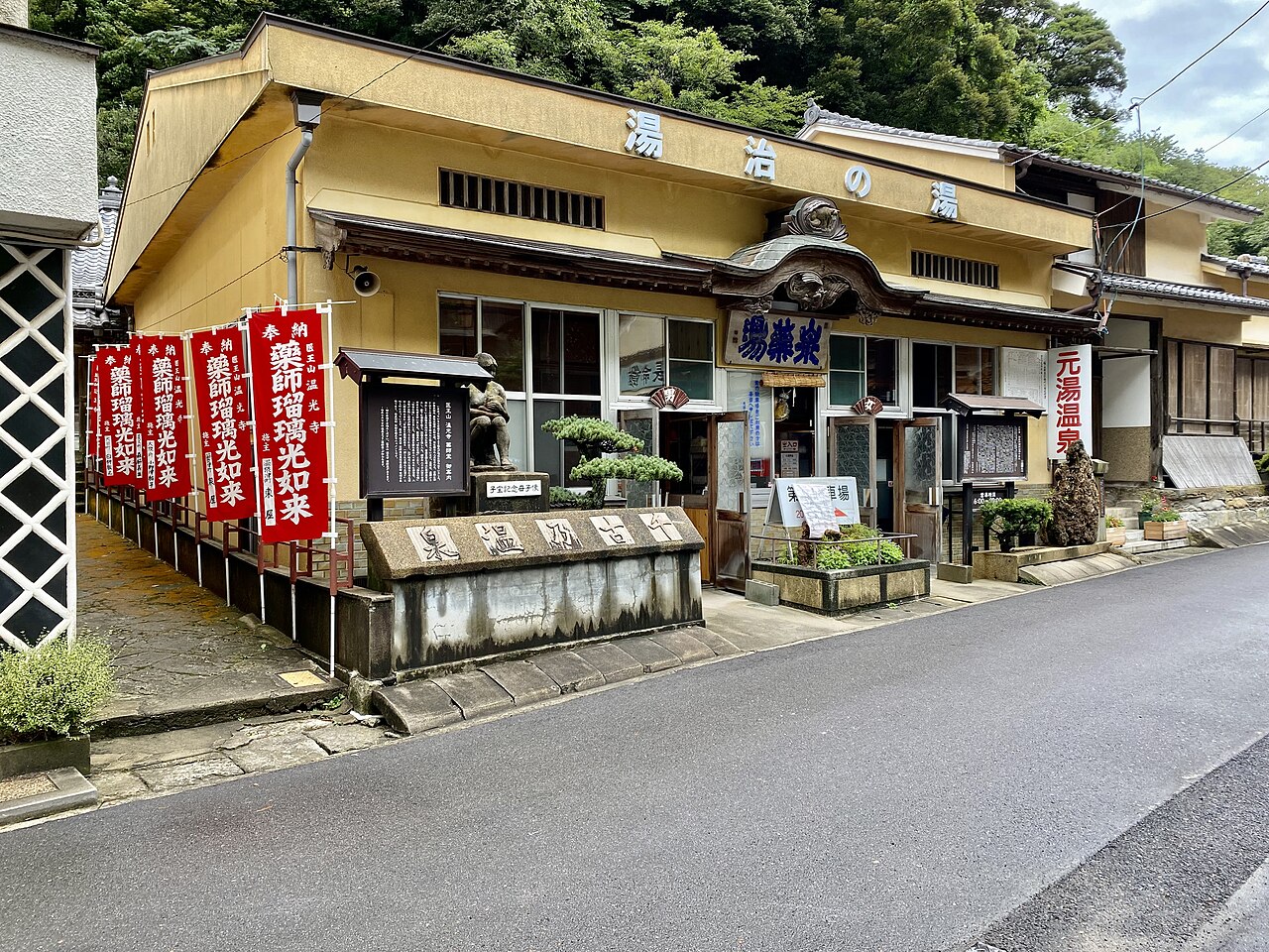 The yellow-fronted Motoyu public bathhouse on the roadside, with red banners and a tiled roof.