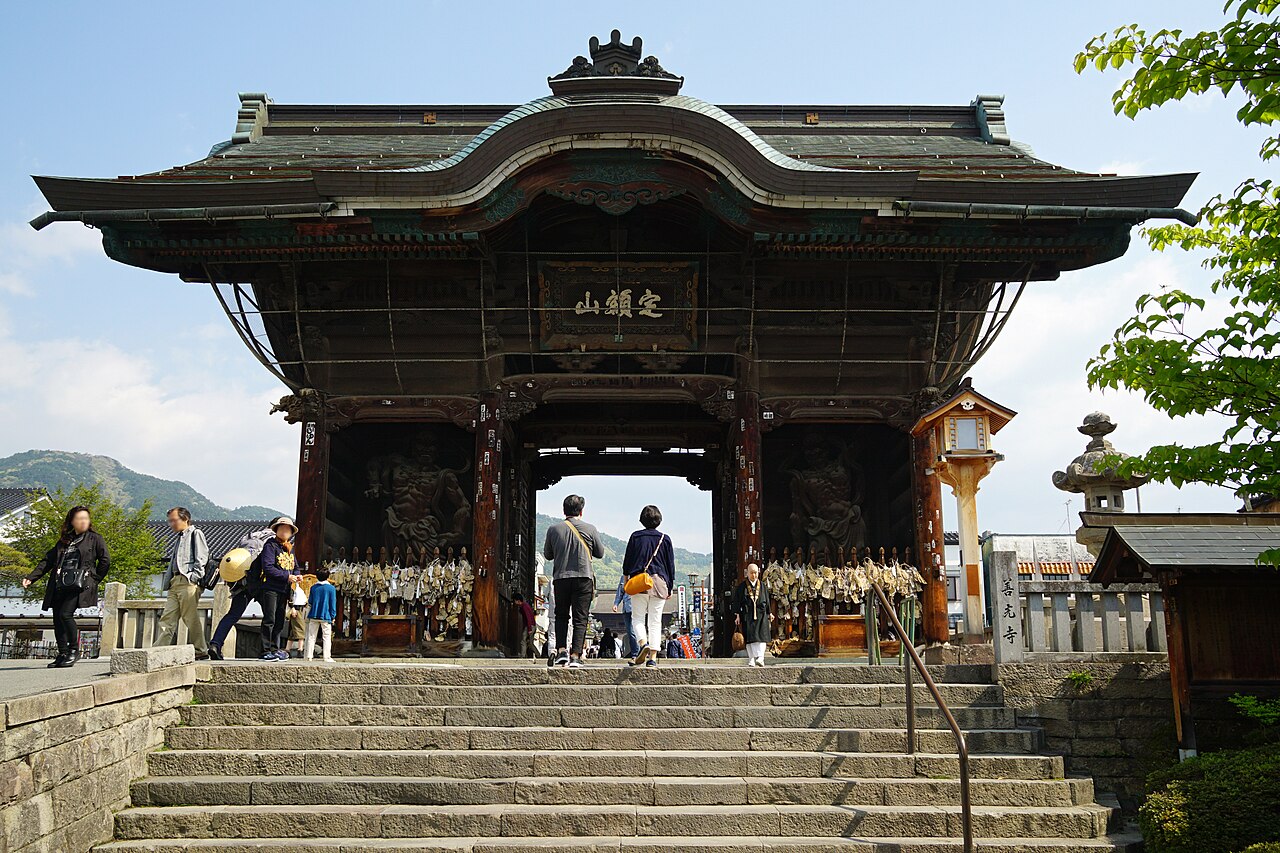 Wooden Niomon gate with a curved green roof and guardian statues on both sides, with visitors on the stone steps in front