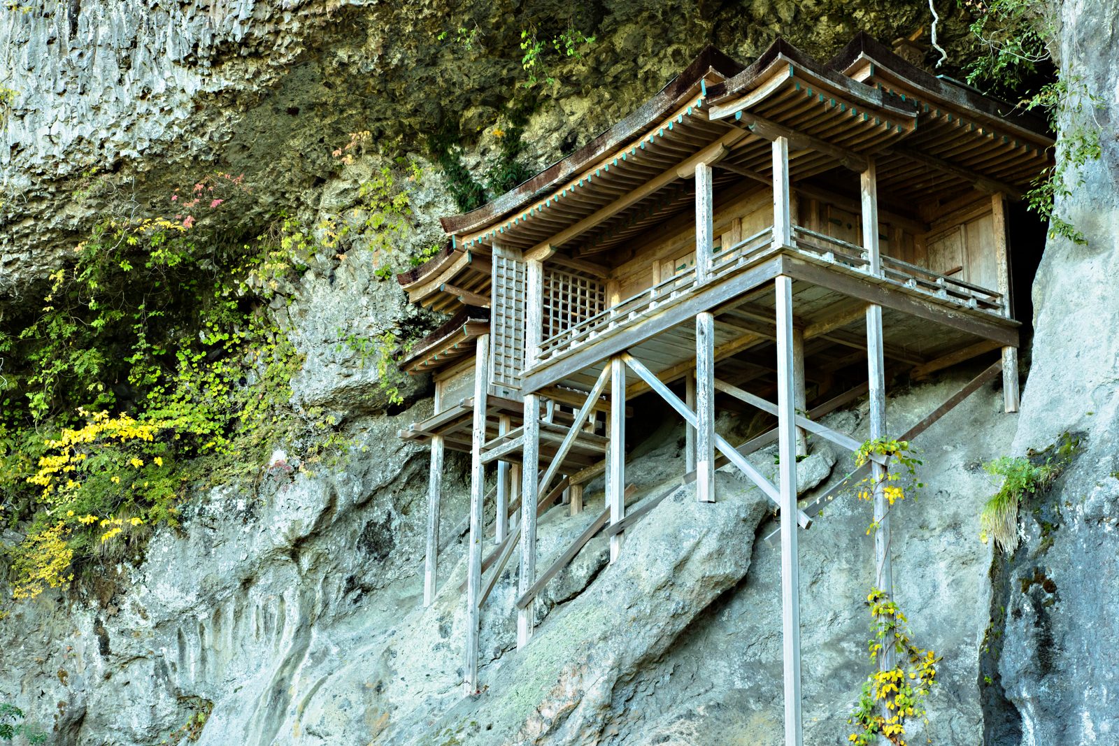 Close view of the Nageiredo hall, its tiled roof and veranda supported by slender wooden pillars against a rock wall