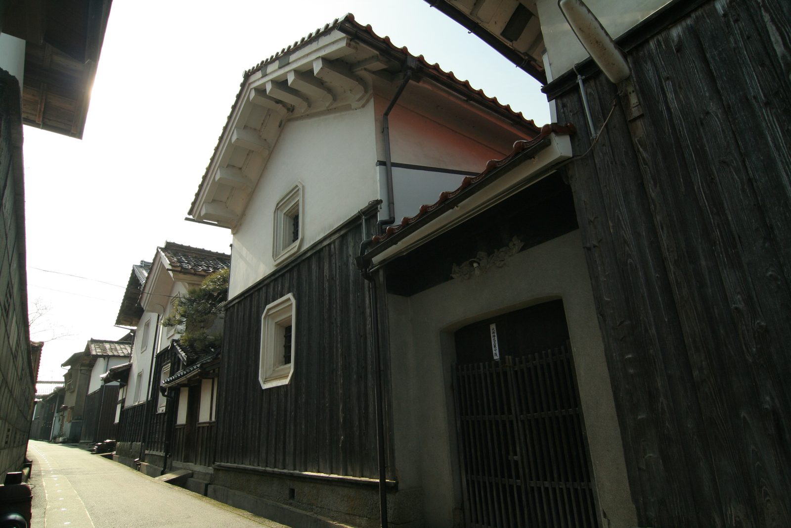 A white-plastered storehouse with deep eaves and a black timber lower wall along a quiet lane in Wakasa