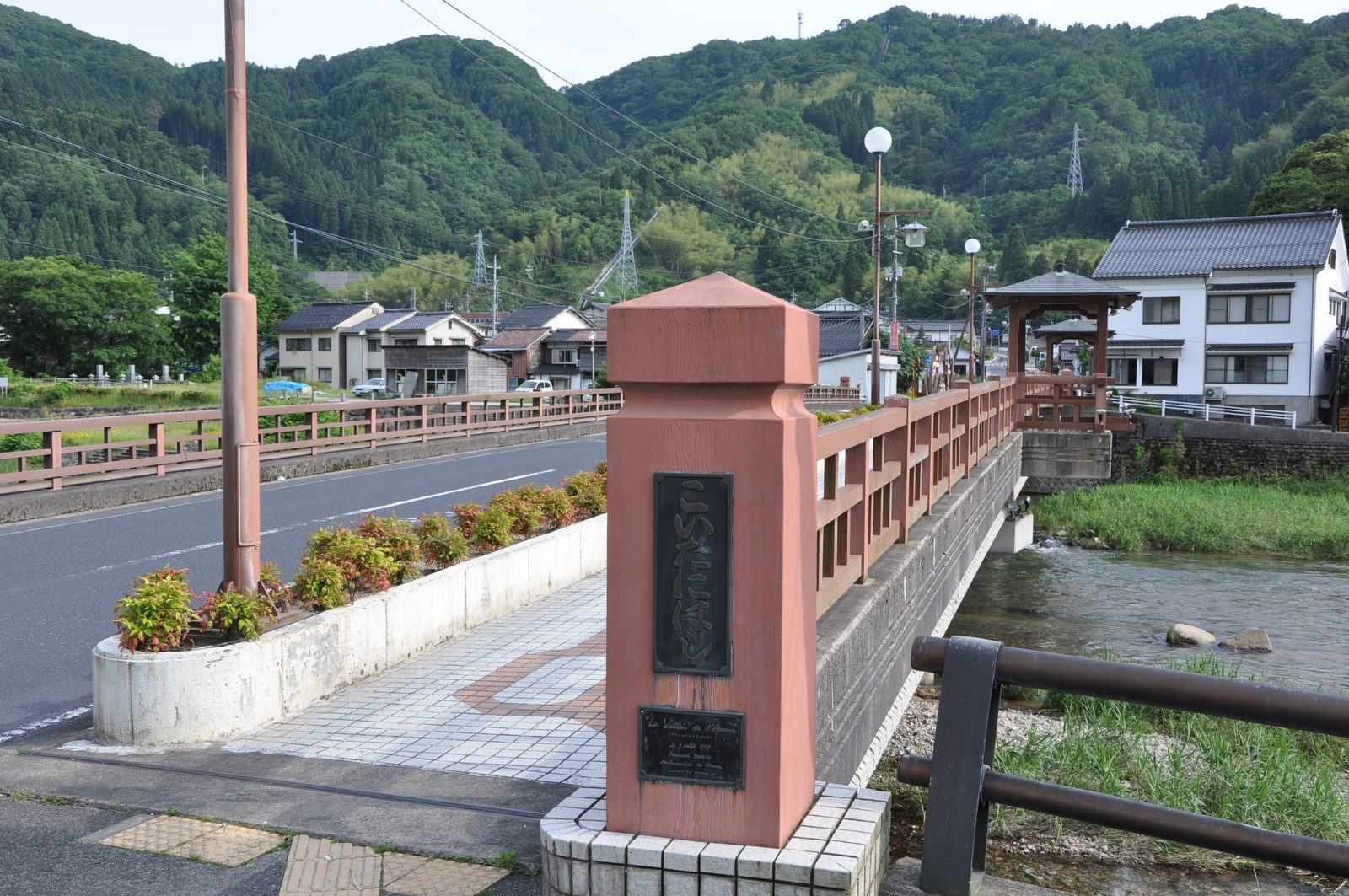 The Koidani Bridge over the river in Misasa Onsen, with a stone pillar at the bridge end and wooded hills behind