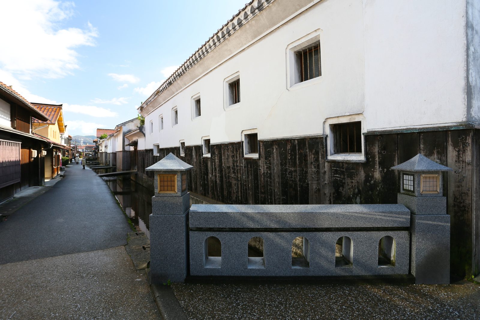 A stone bridge with two stone lanterns in front of white-walled storehouses on the Tamagawa canal