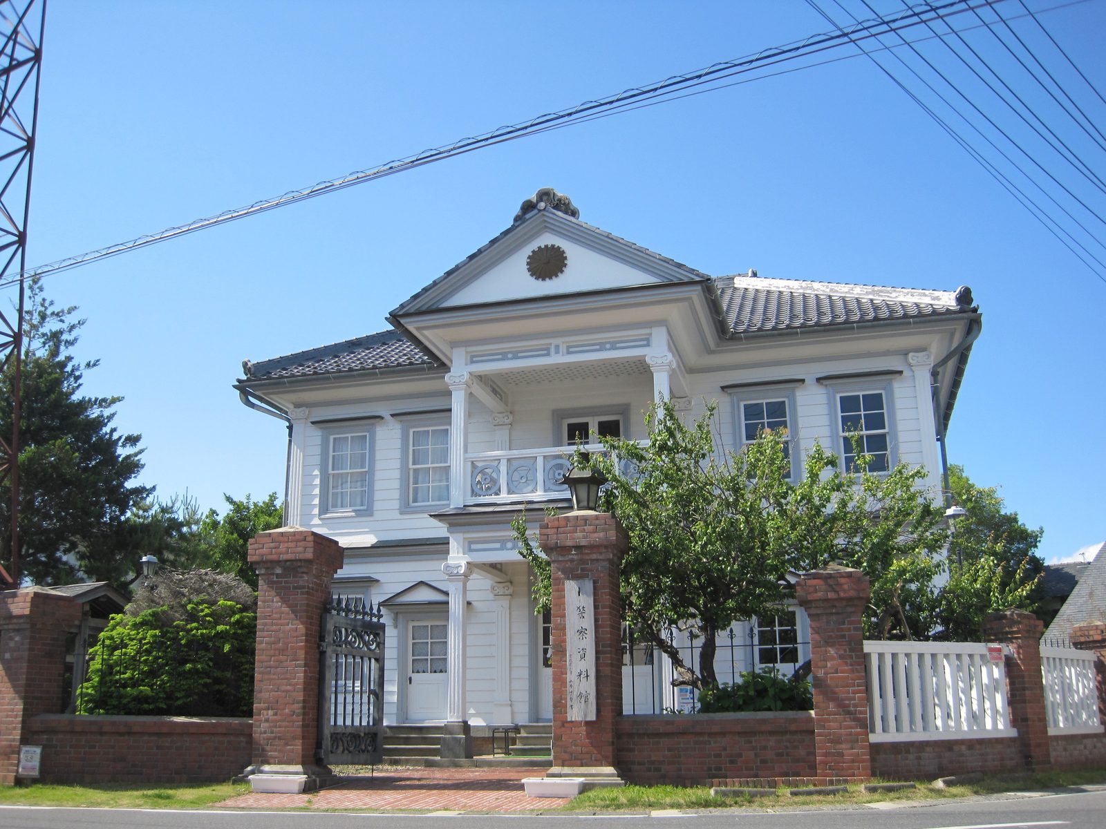White two-story Western-style former police station with brick gate posts and a sign.