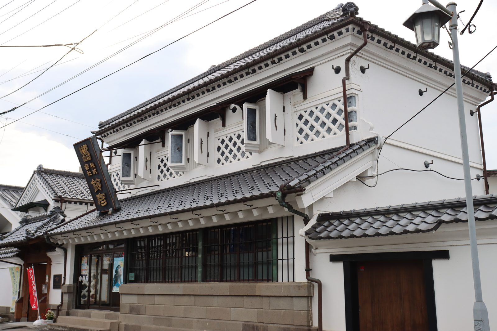 Grey-plastered two-story merchant building with lattice windows on a traditional street.