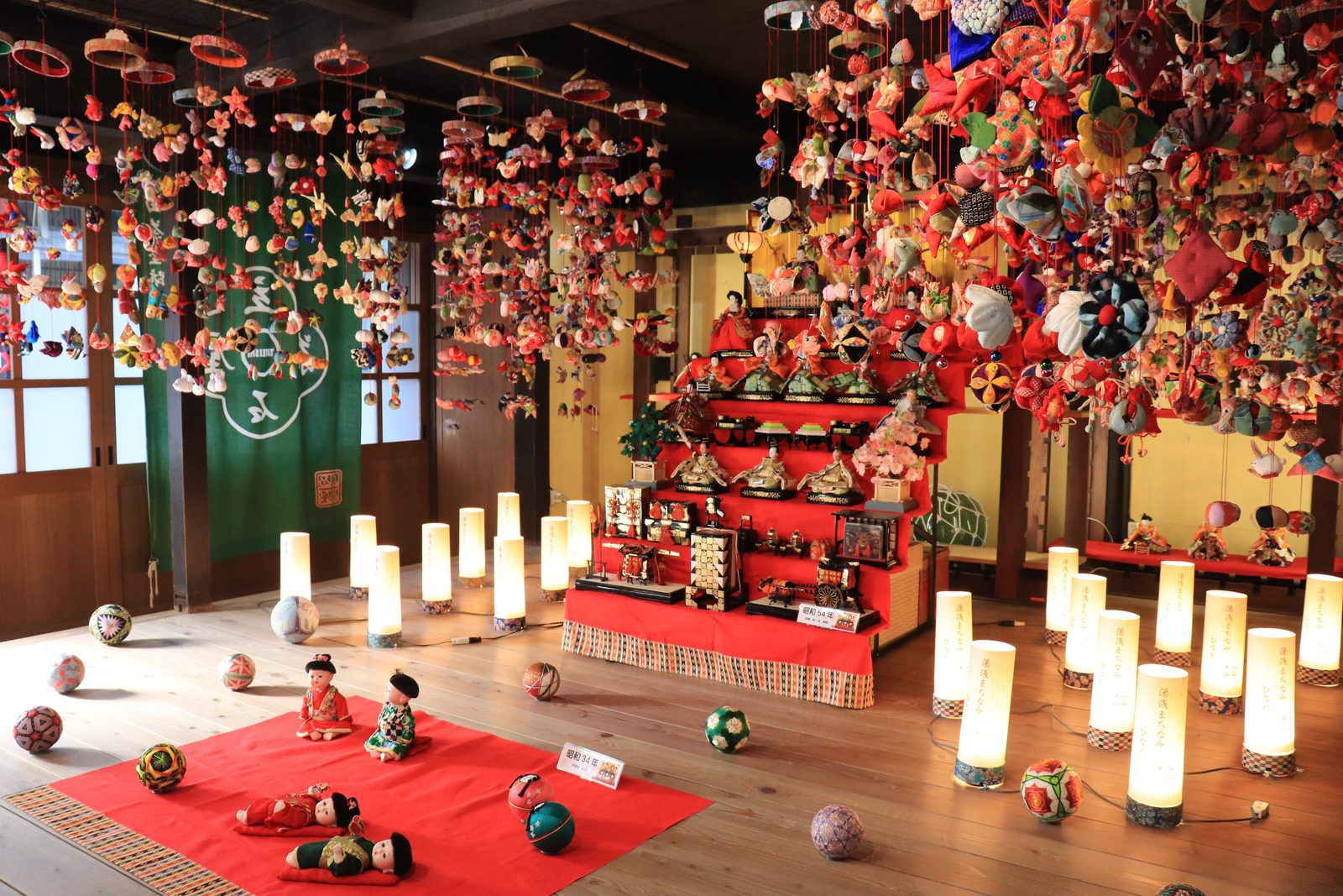 Tiered hina dolls and colourful hanging ornaments displayed with candle lights inside an old wooden building in Yuasa