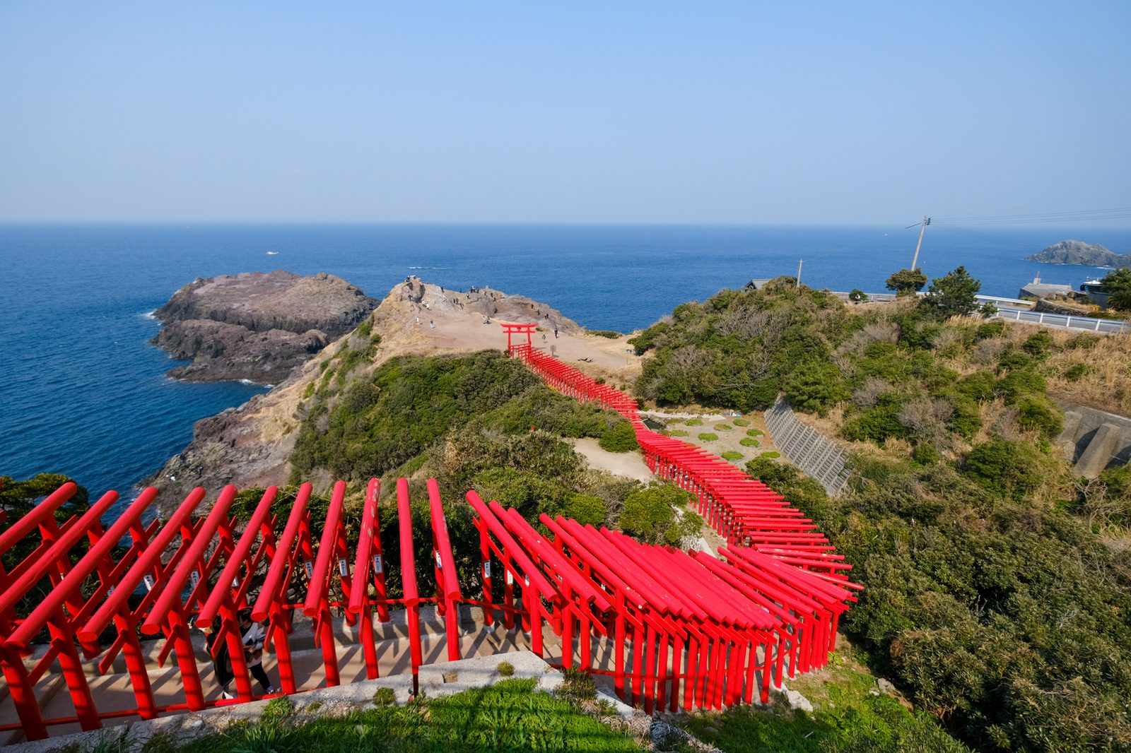 Red torii gates of Motonosumi Shrine winding down a green slope toward the sea in Nagato