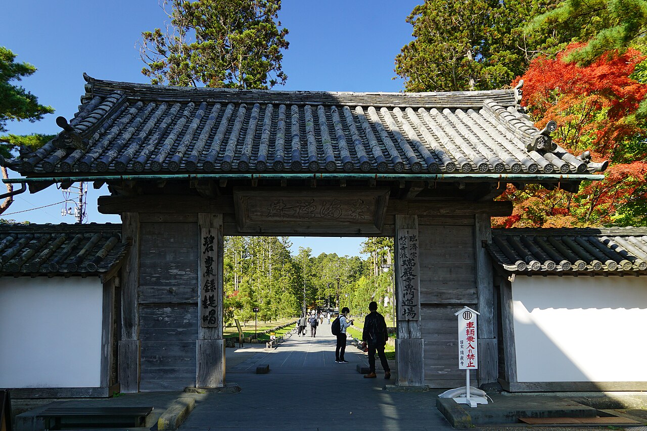 The wooden main gate of Zuiganji, with a cedar-lined avenue running away beyond it and maples colouring at the right